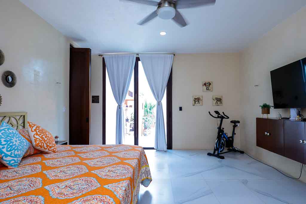 Bright bedroom with a balcony and exercise bike.