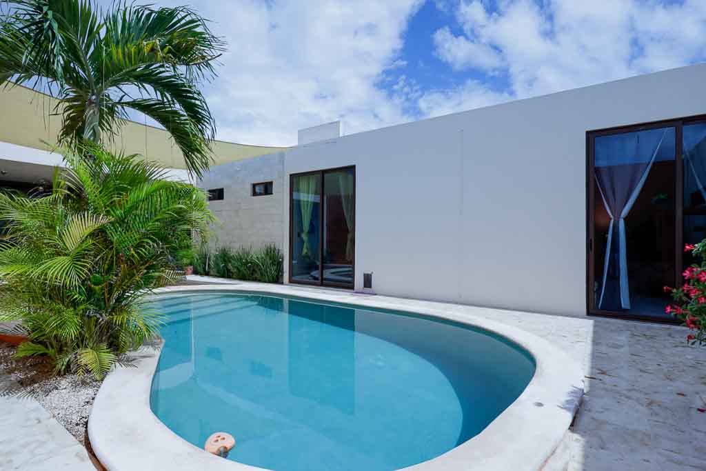 Modern white house with a curved swimming pool under a blue sky.
