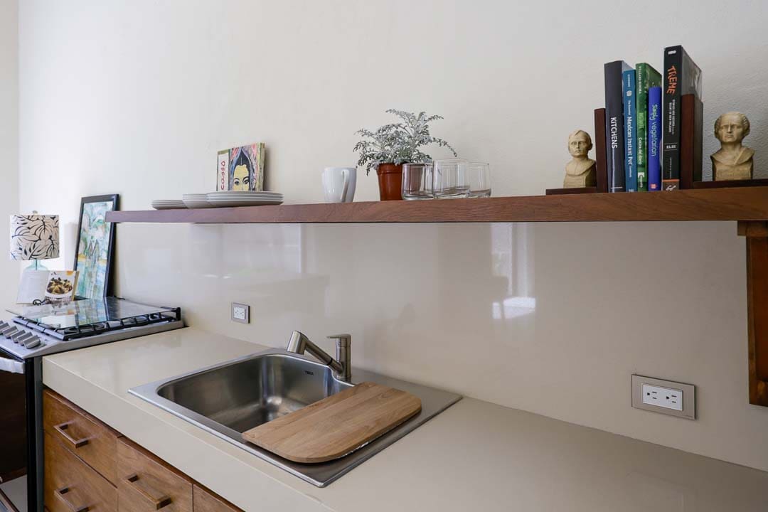 Minimalist kitchen sink area with wooden shelves and plants.