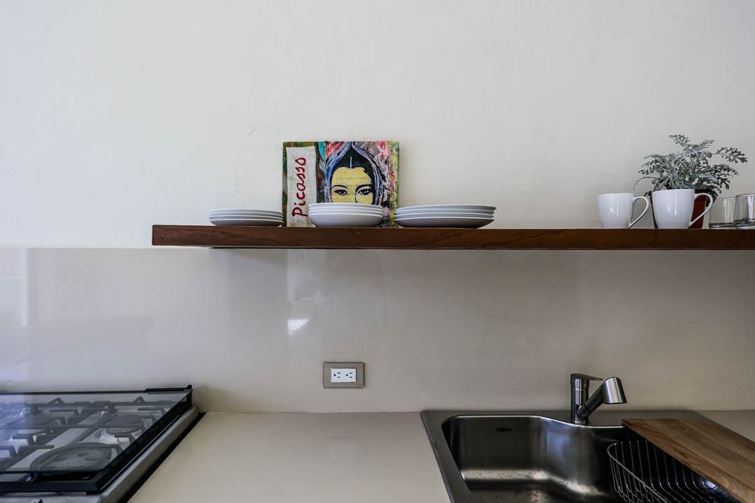 Minimalist kitchen counter with a wooden shelf holding a framed photo and a few dishes.