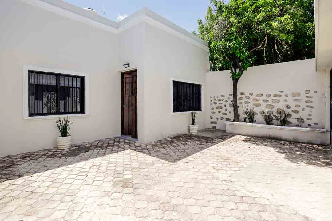 White building with a wooden door and black window bars in a sunny courtyard.