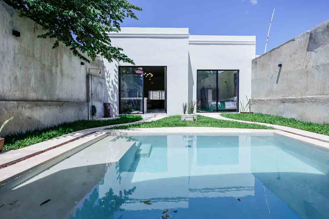 Modern white house with a pool and green lawn under a clear blue sky.