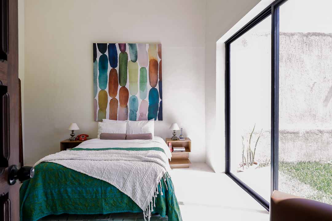 Minimalist bedroom with colorful abstract art and large window.