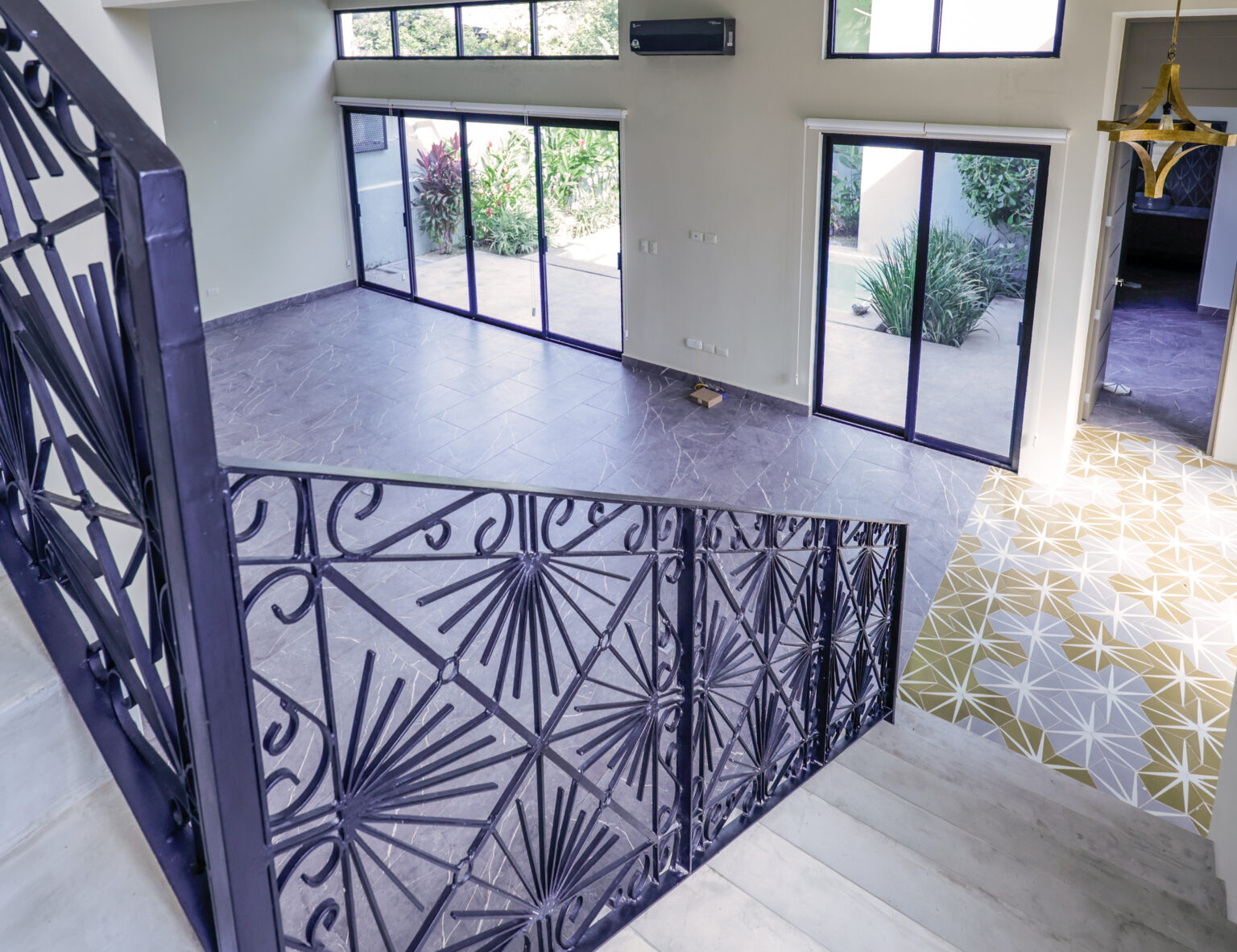 Modern staircase with decorative wrought iron railing and large windows.