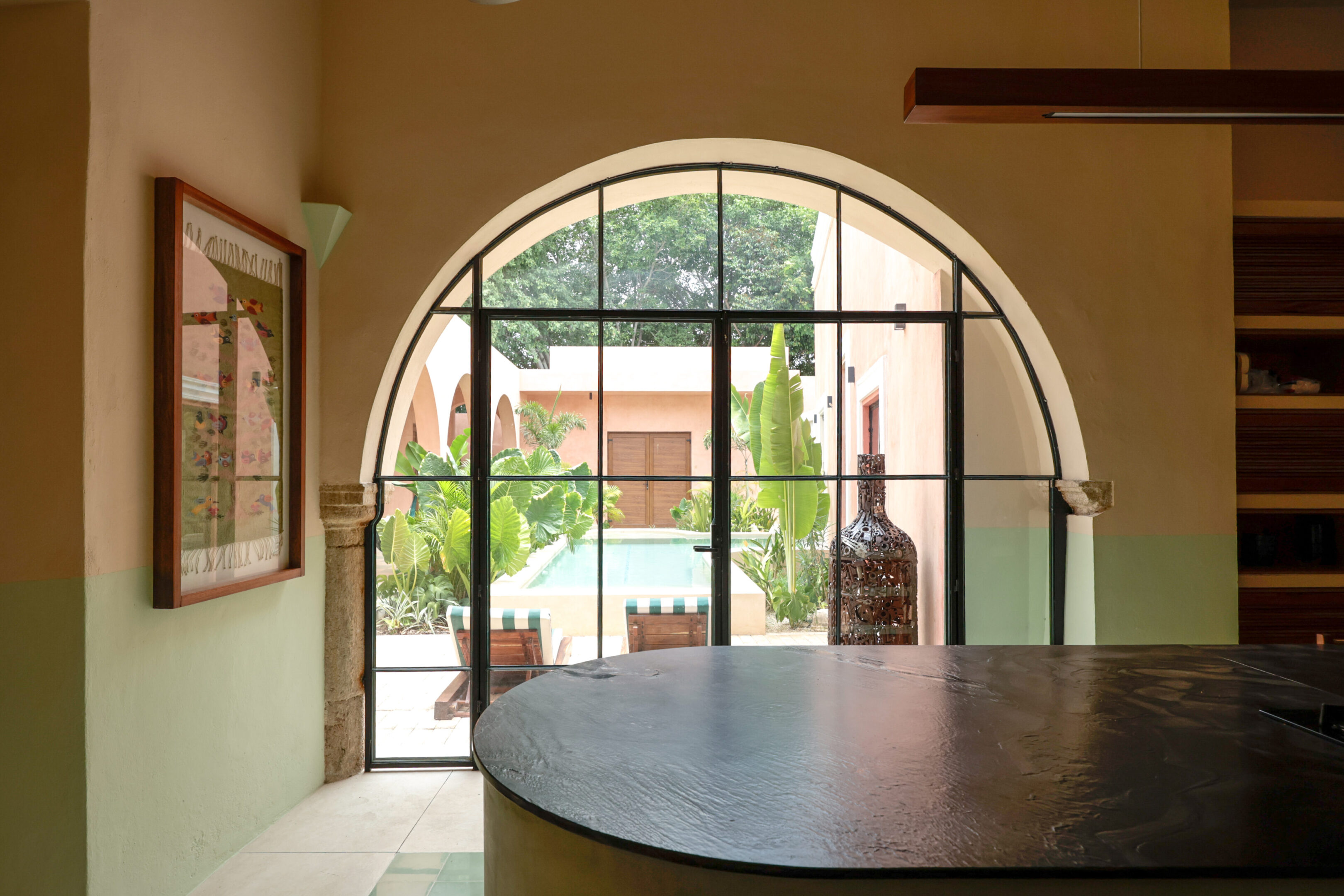 View through a large arched window into a courtyard with greenery.