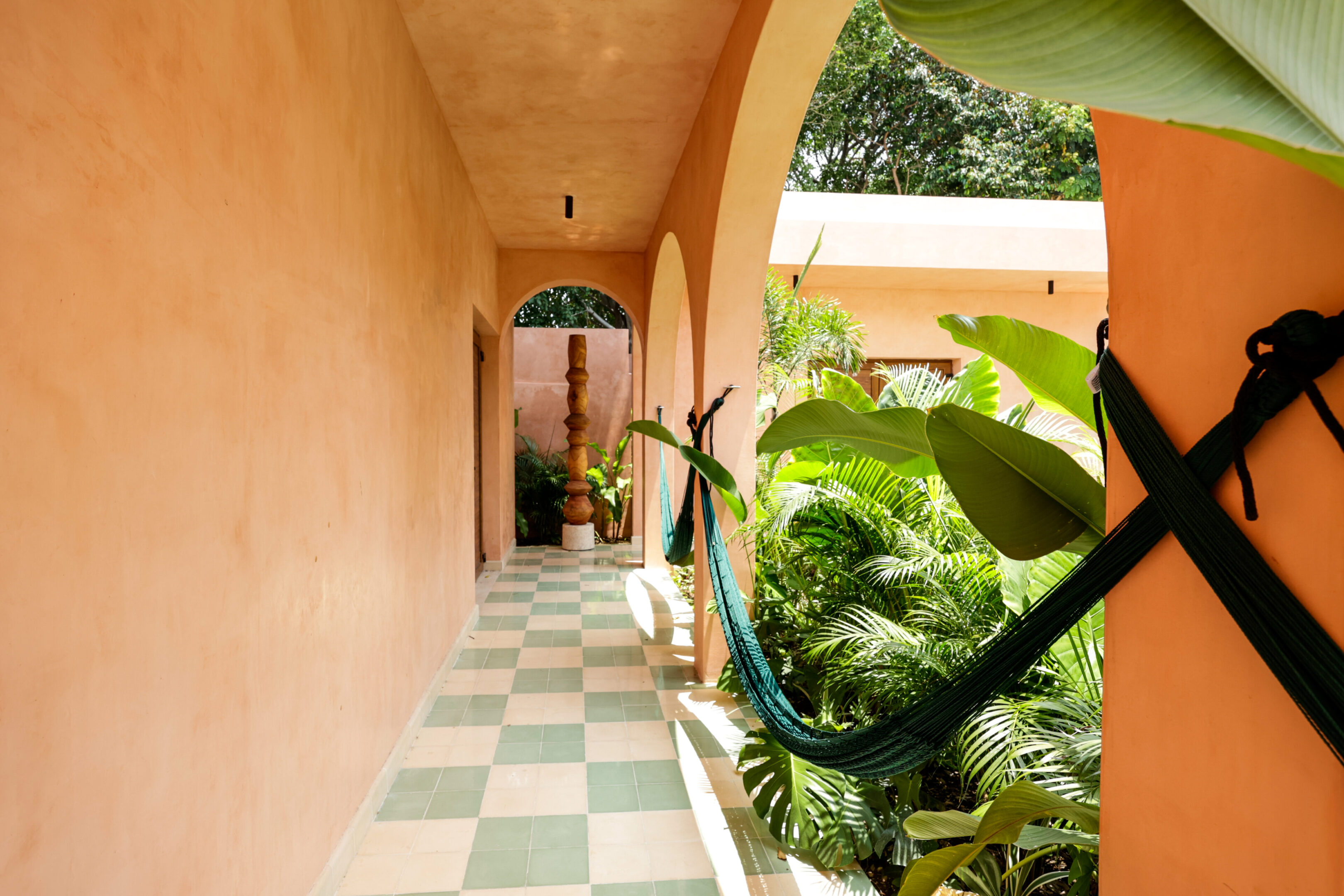 Sunlit corridor with lush green plants and a checkered floor.
