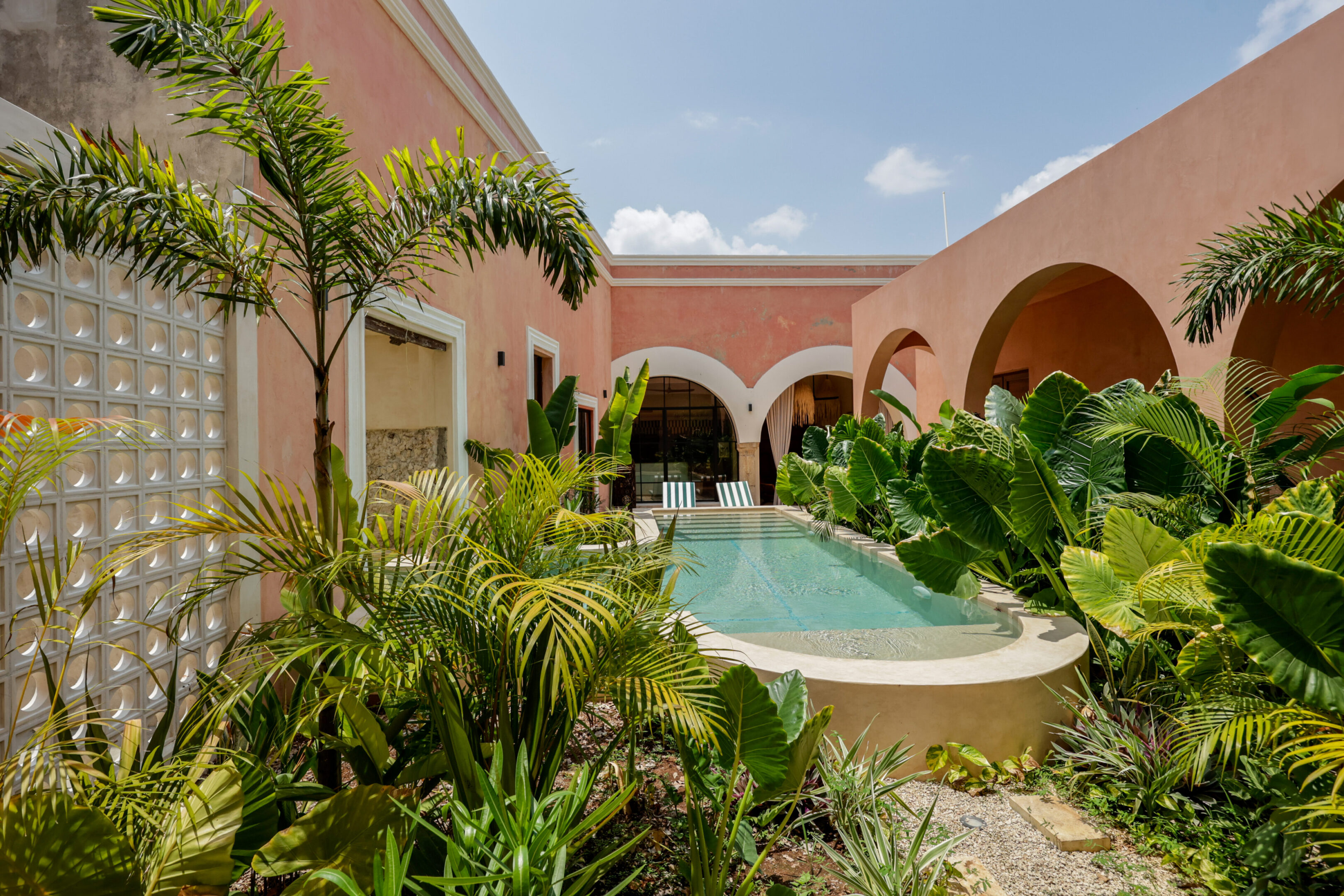 A serene courtyard with a pool and lush greenery under a bright sky.