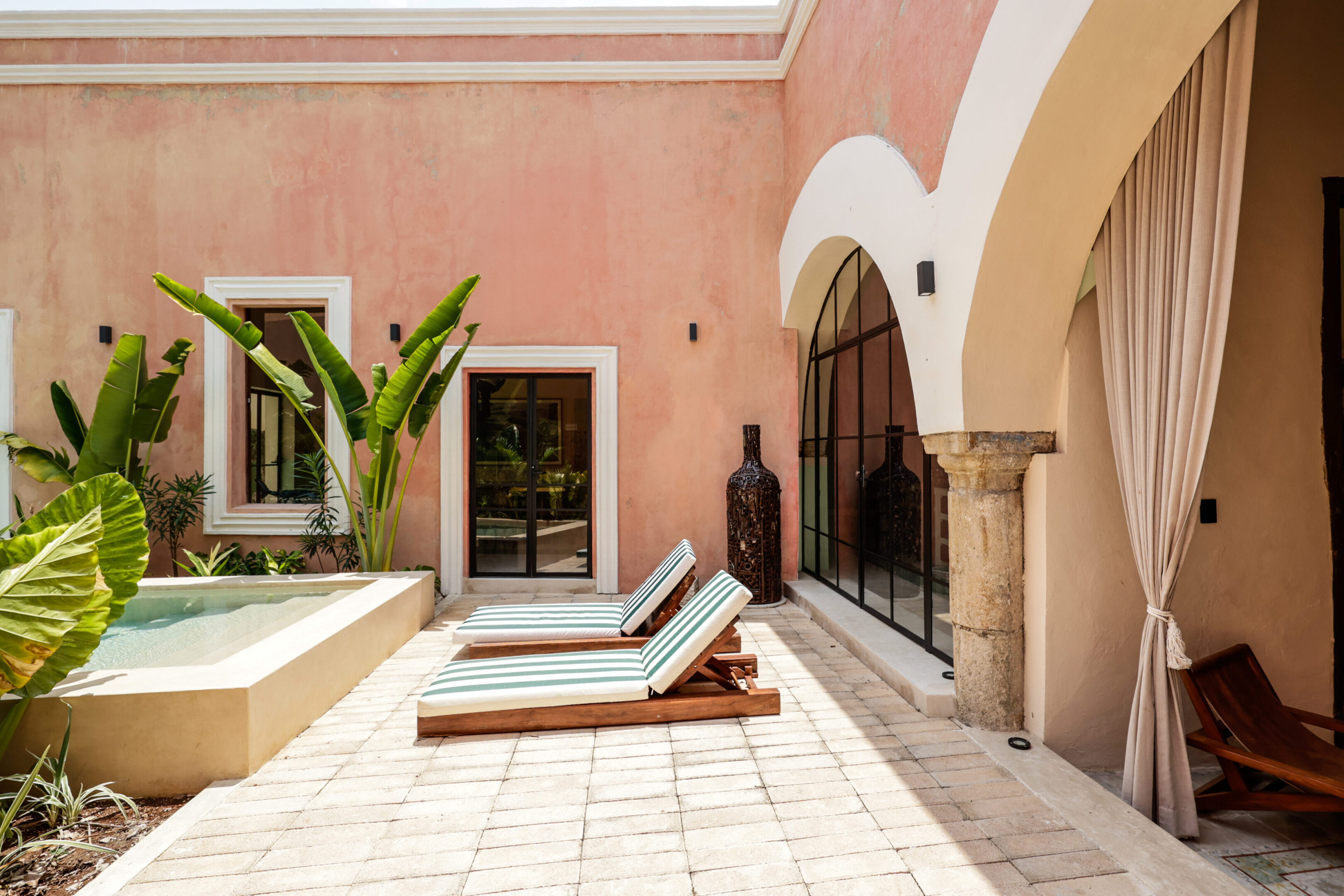 Sunlit patio with lounge chairs and tropical plants under arches.