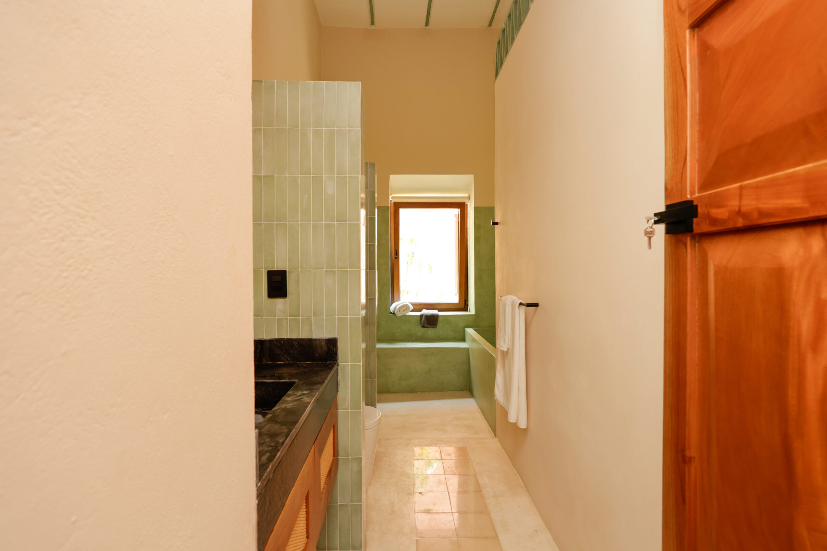 Narrow bathroom with a green bathtub and wooden accents.