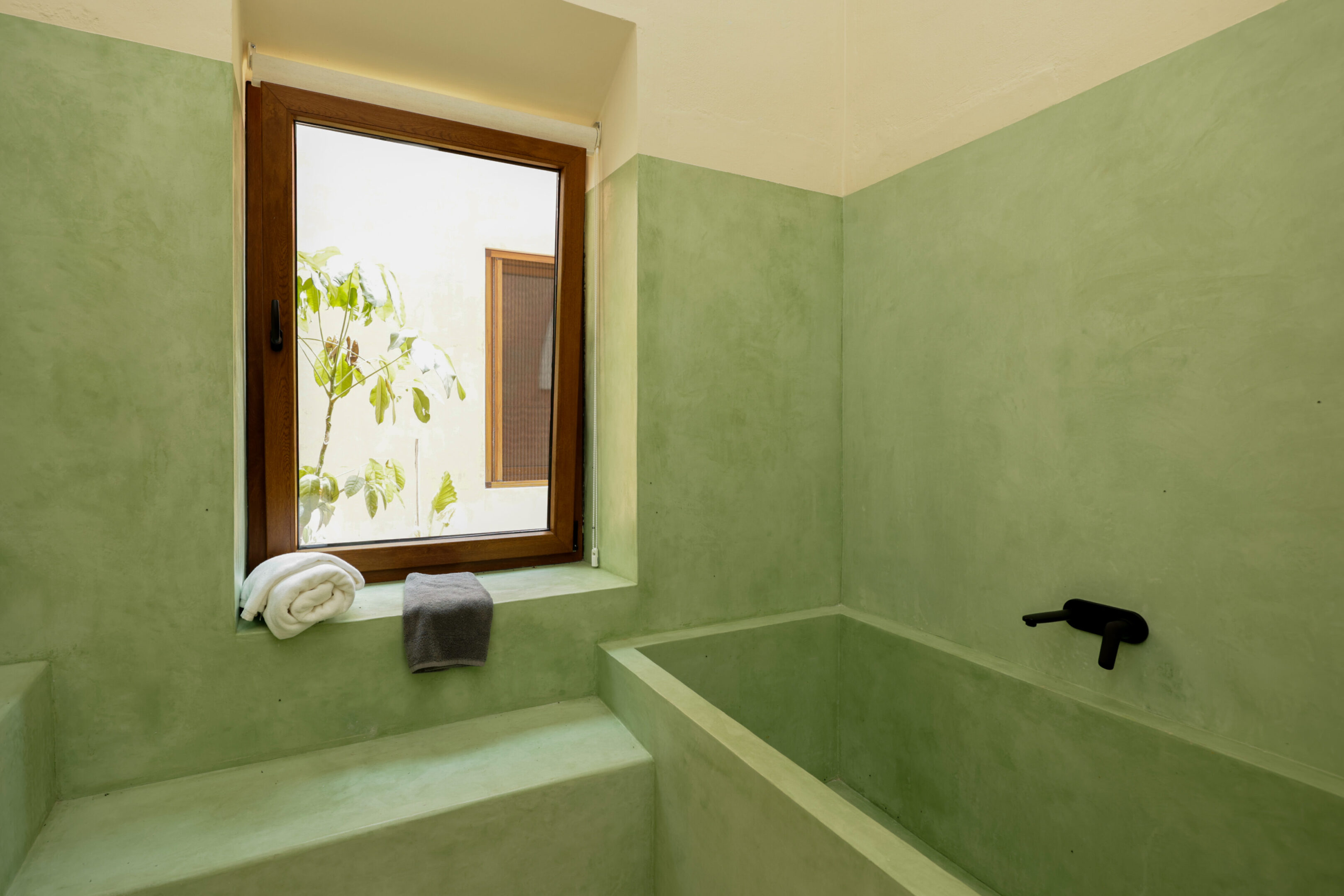 Minimalist bathroom with green tiles and a wooden-framed window.