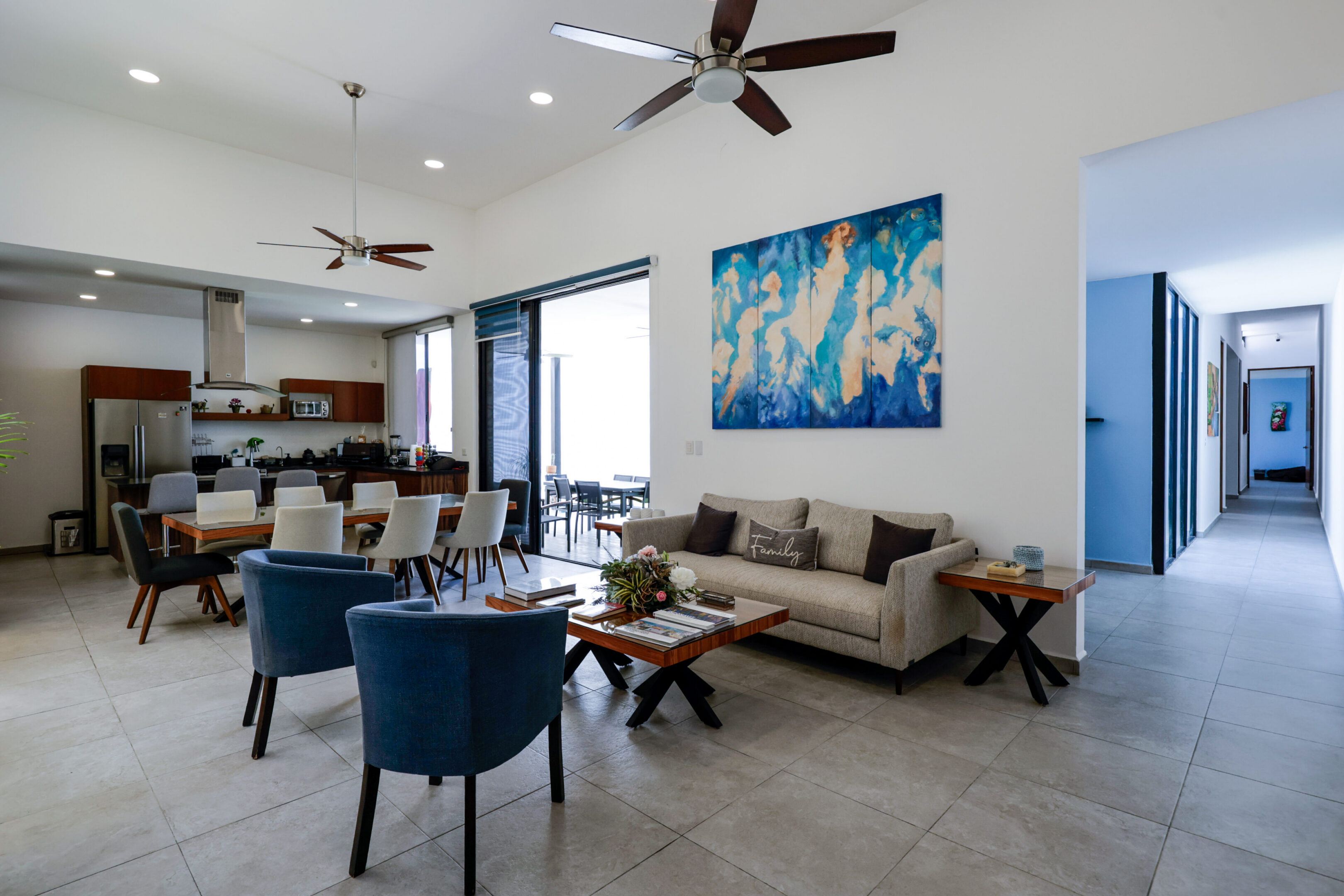 Modern living room with beige sofa and blue chairs under ceiling fans.