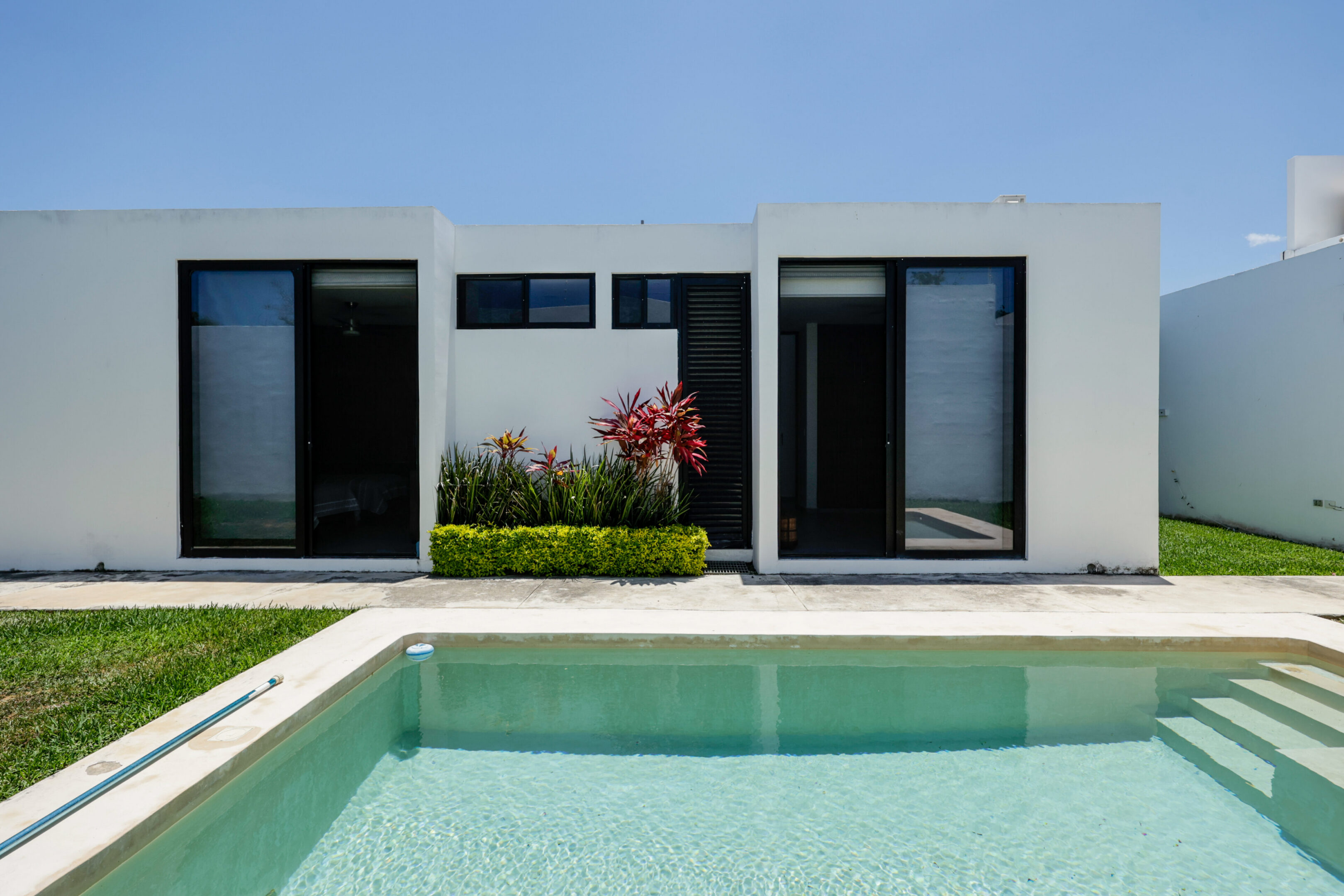 Modern house with large windows and a pool under a clear sky.