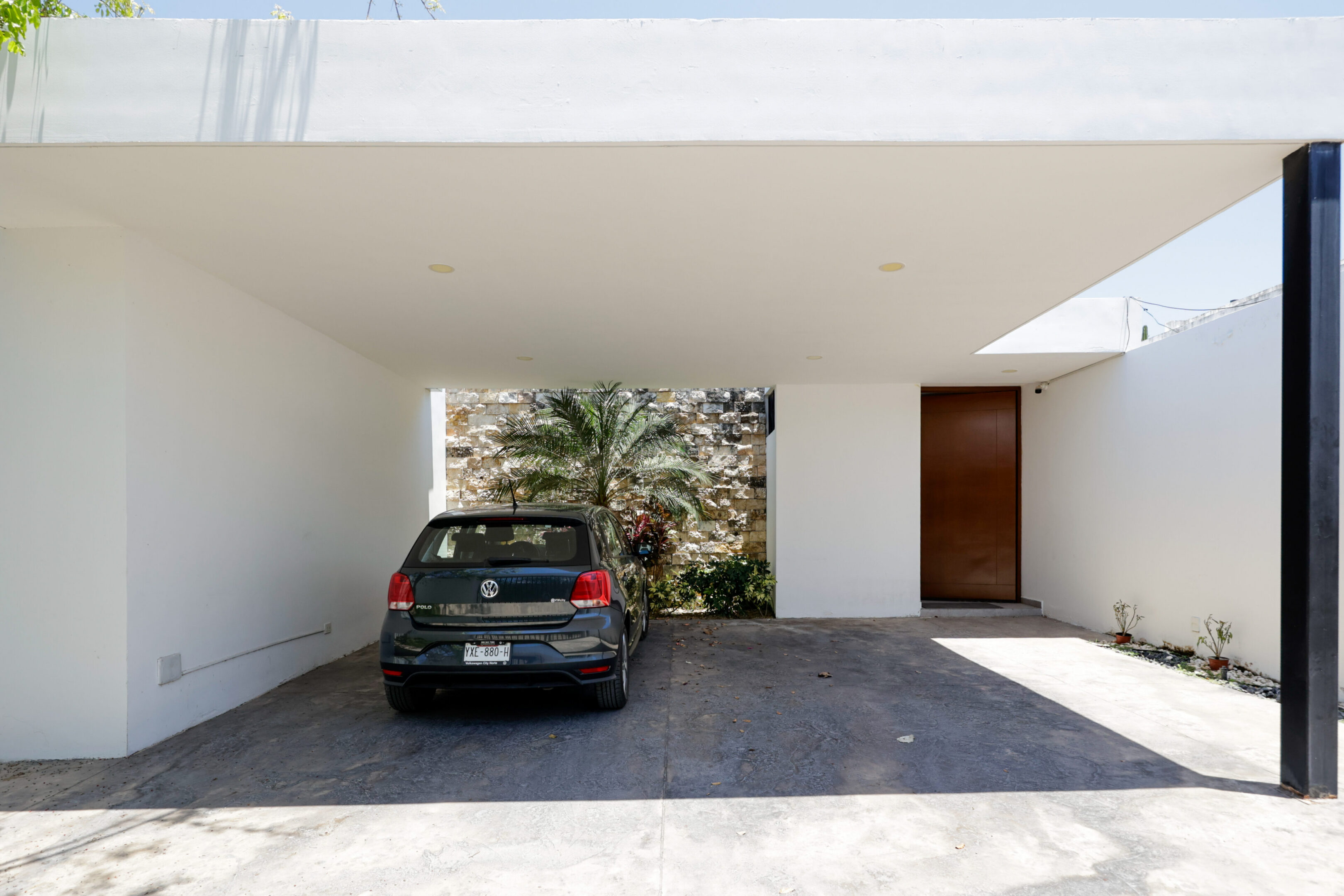 Modern house entrance with a parked black car under a white canopy.