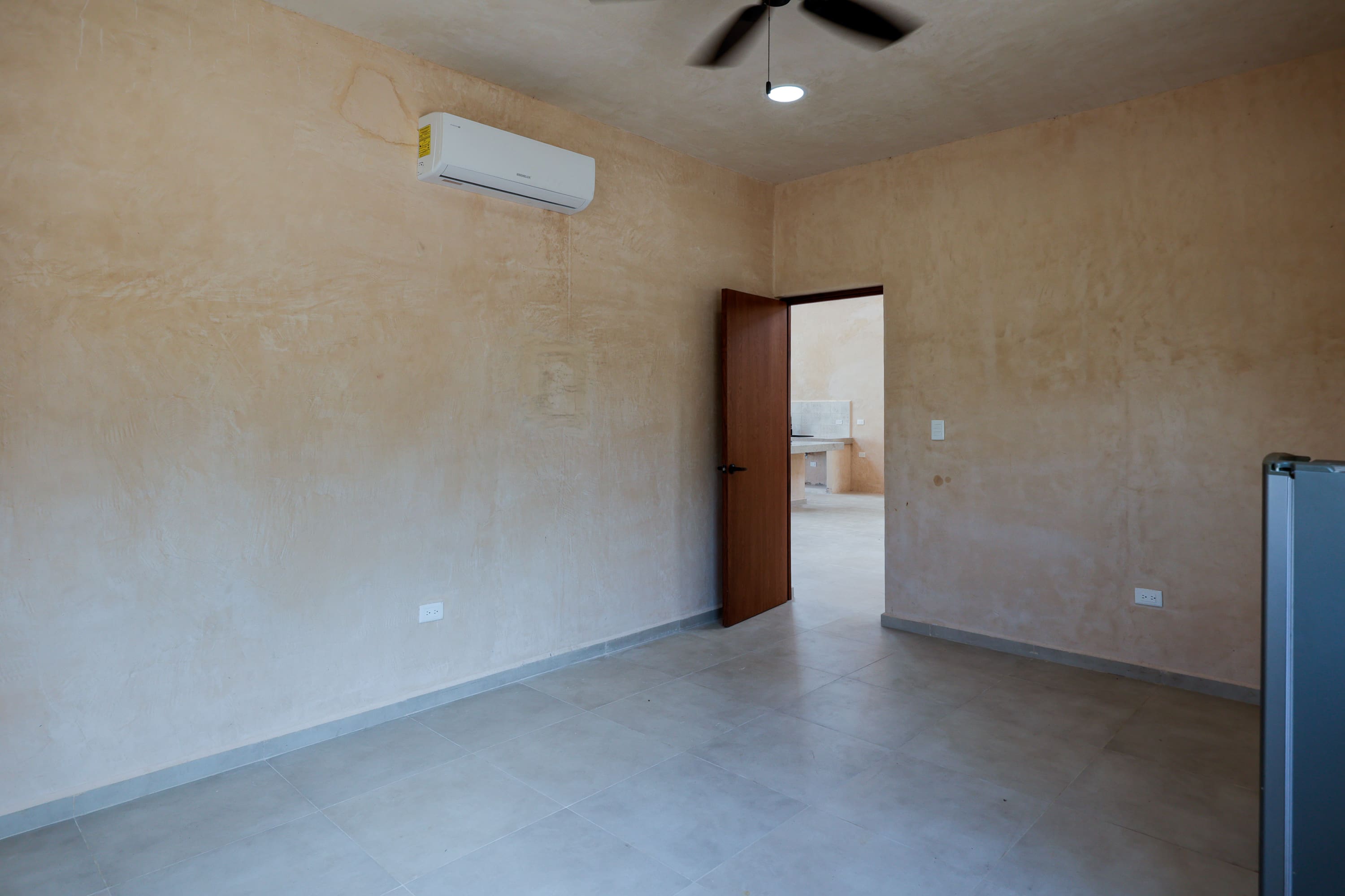 Empty beige room with split AC and fan