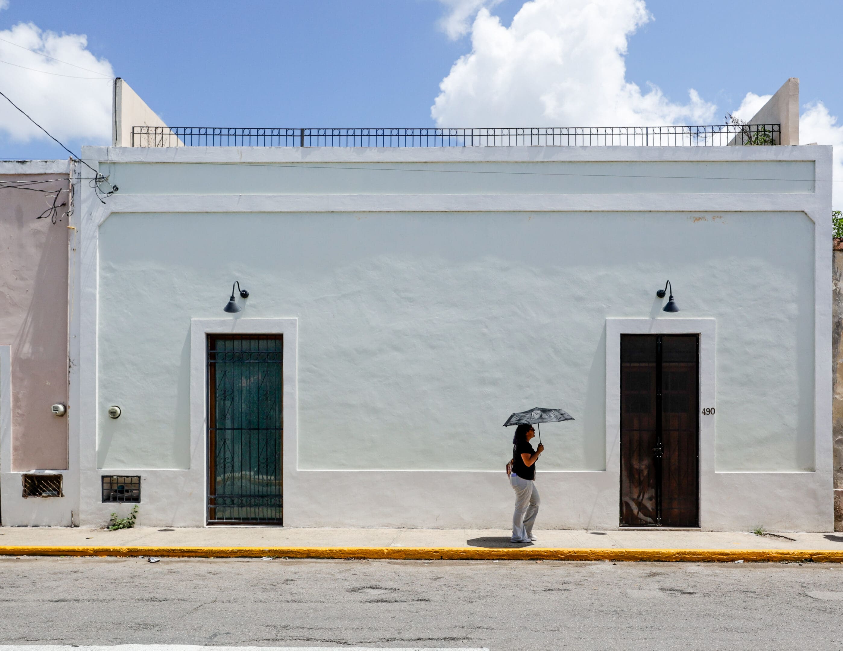 Person with umbrella walking past white building